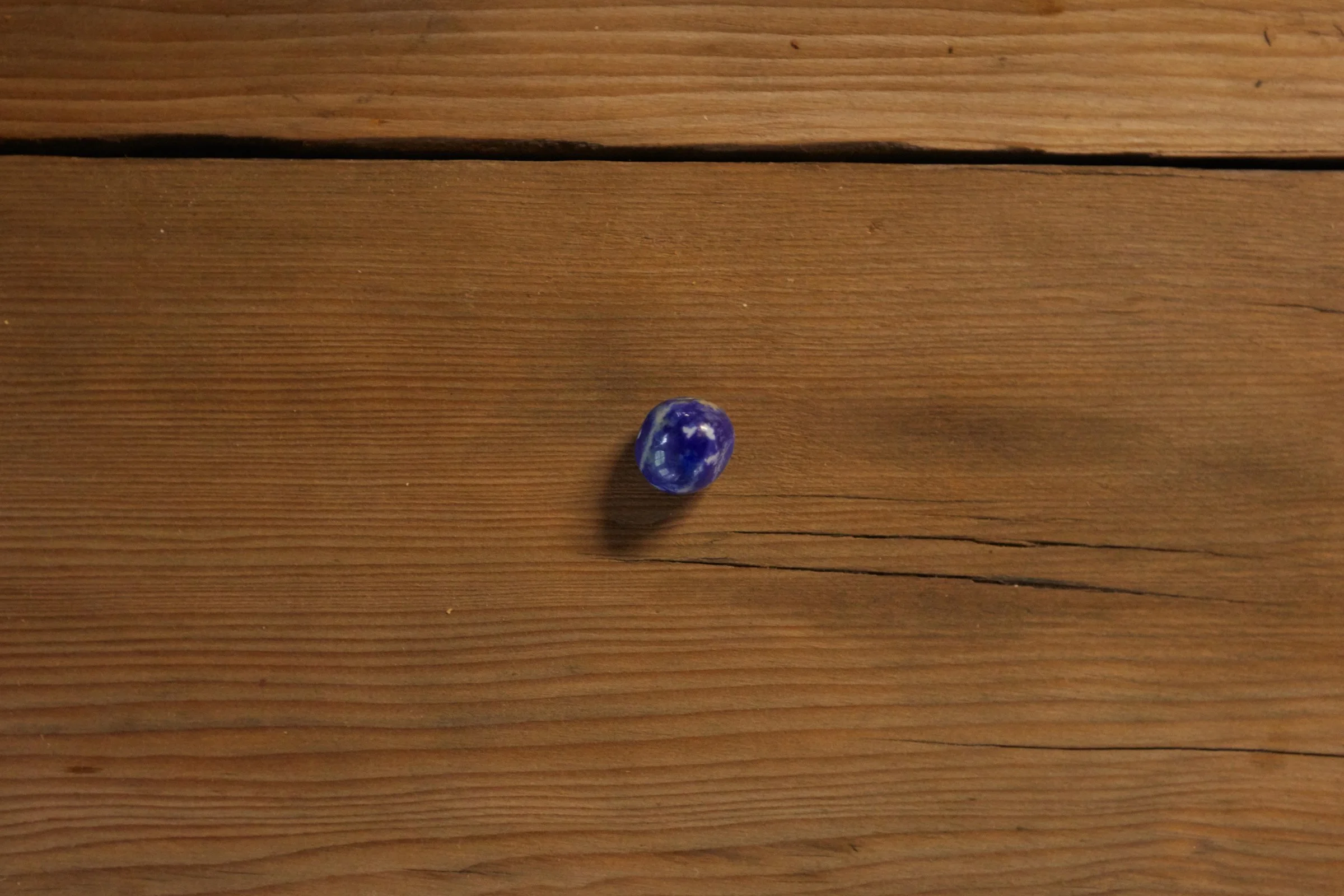 Close up of a small blue with white swirlies in it marble ball on a wooden desk.