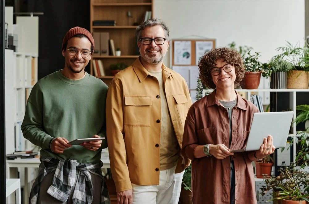 A smiling team of digital marketing and website design professionals standing together in a modern office environment, serving Inland Empire businesses.