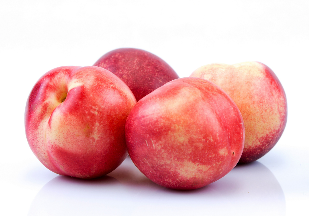 Four fresh peaches with red and yellow skin on a white background.