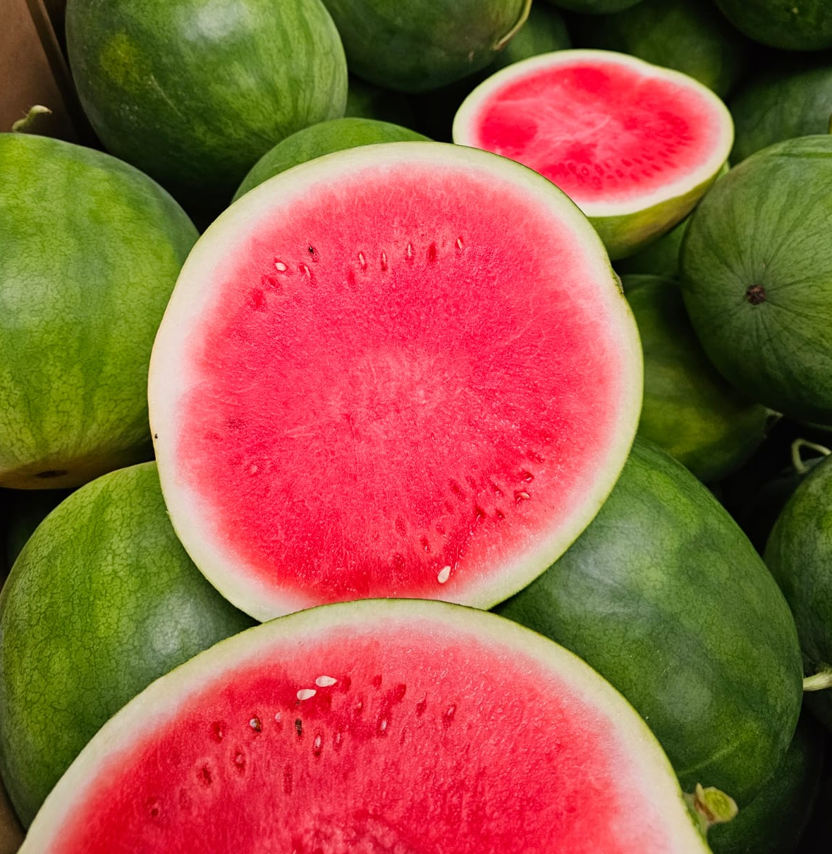 Watermelons, including some cut open to show the pinkish-red flesh with black seeds.