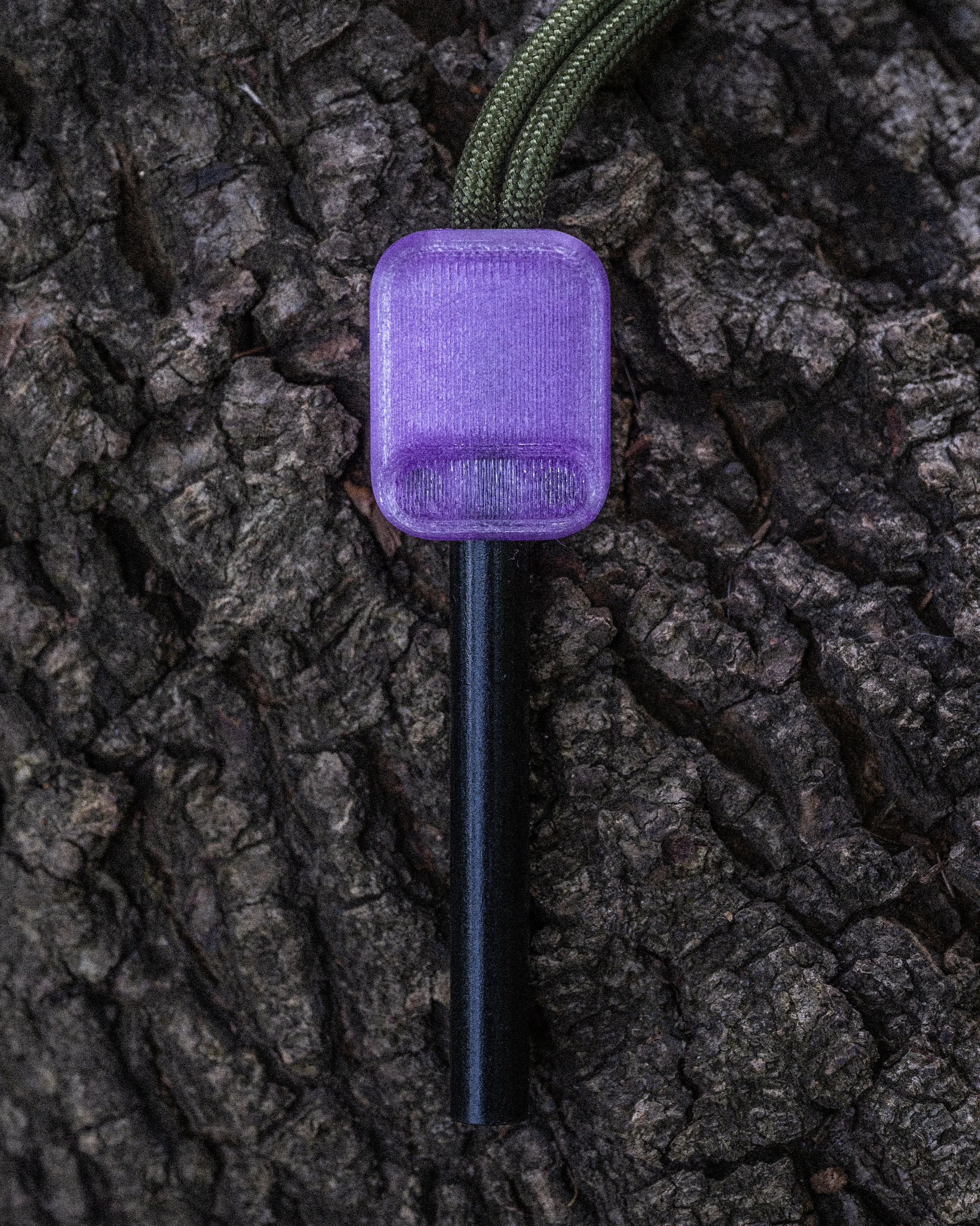 A purple GPS device connected to a green lanyard, lying on rough, dark bark.