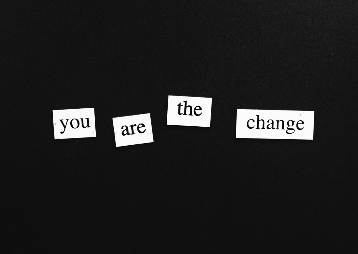 Black background with cut-out paper words spelling "you are the change" arranged in a curved line.
