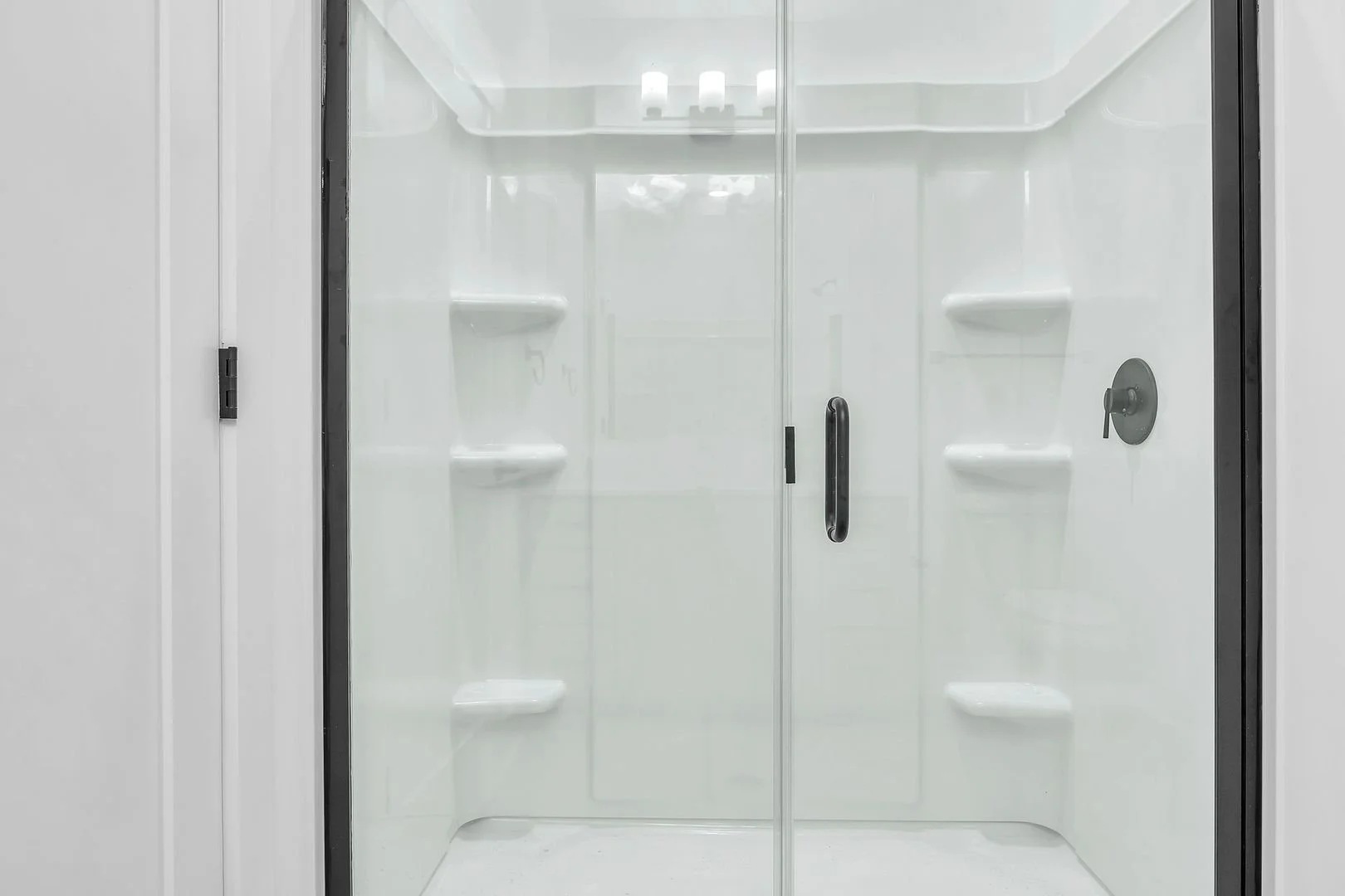 Empty white shower stall with glass door, built-in shelves, and a showerhead.