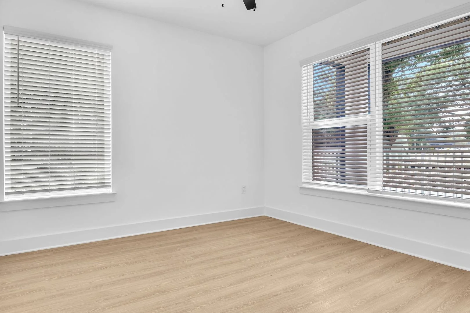 Empty white room with wooden flooring and large windows with white blinds