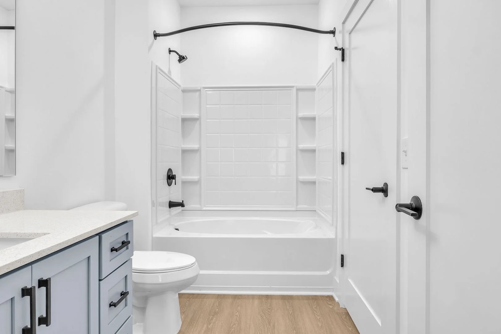 Clean white bathroom with a bathtub and shower combo, blue vanity with black hardware, and wood flooring.