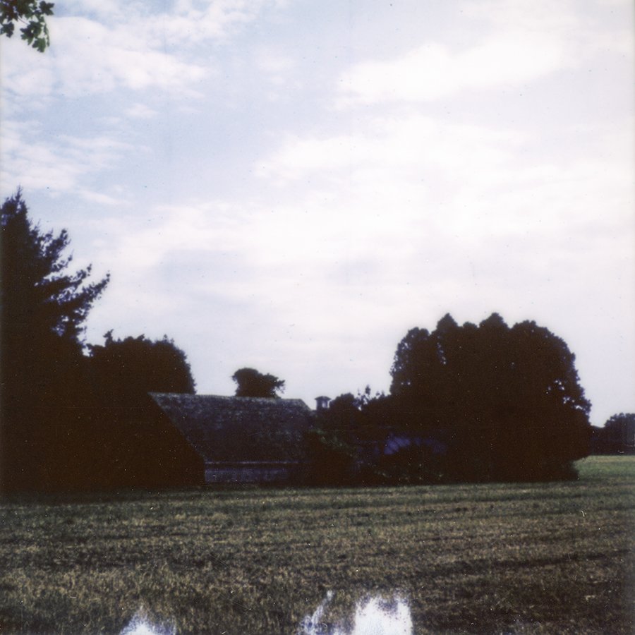 a polaroid of an old farmhouse next to a farmer's field