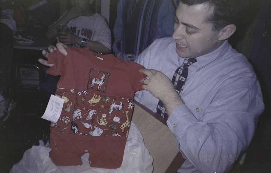 a man holds a red onesie at a baby shower in 1998.