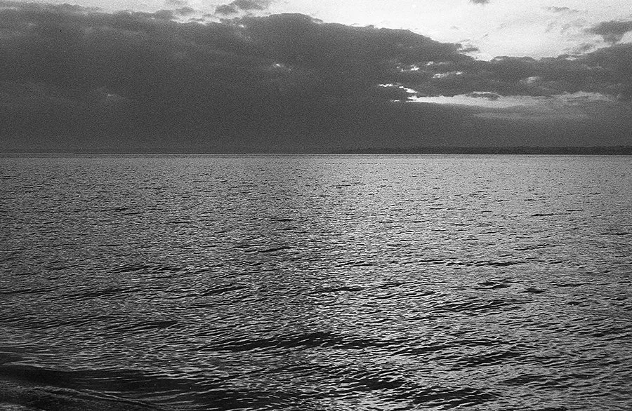 a black and white photograph showing the ocean at dusk with a dark cloud bank over it