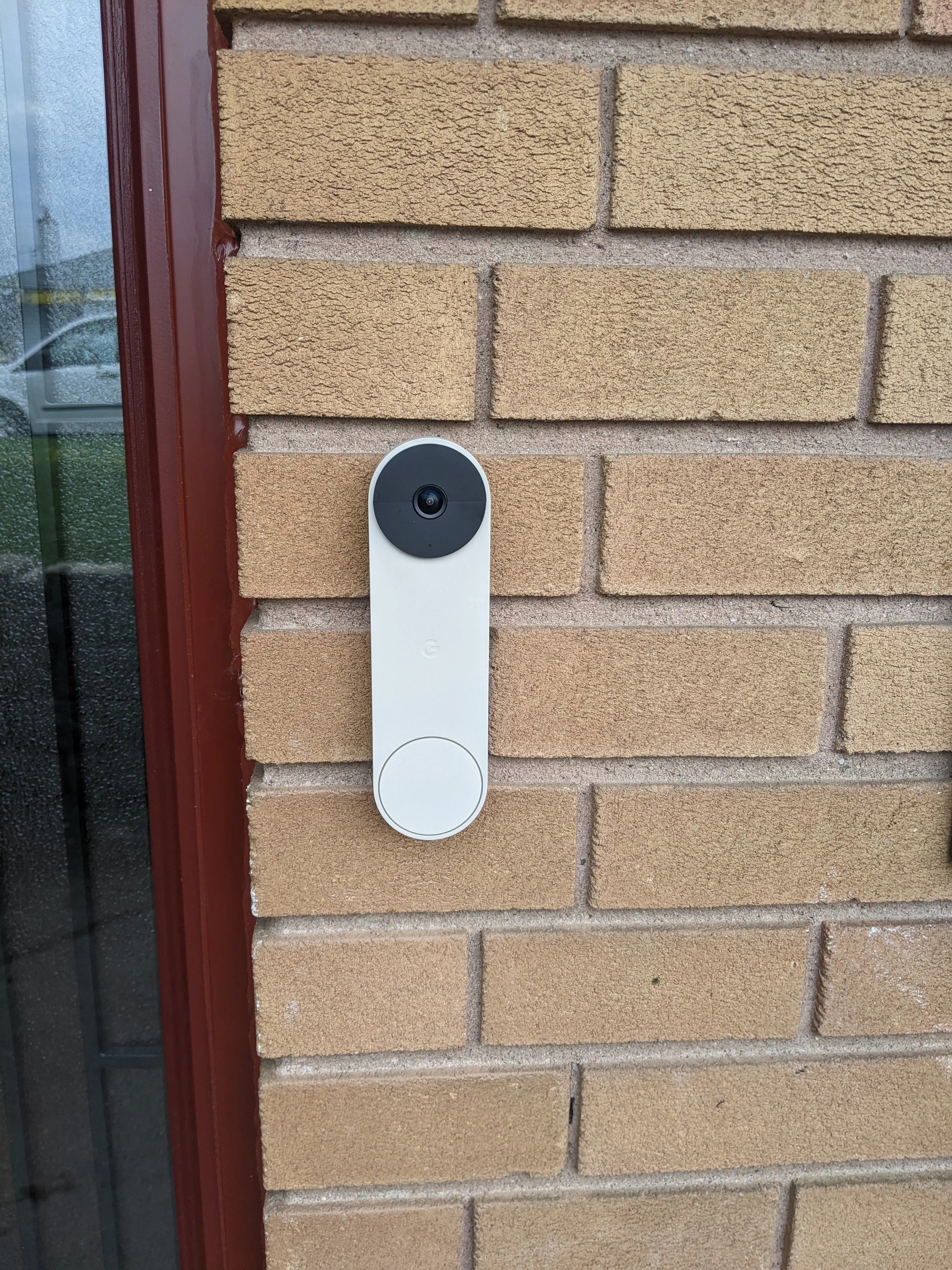 A doorbell camera mounted on a brick wall next to a glass door.