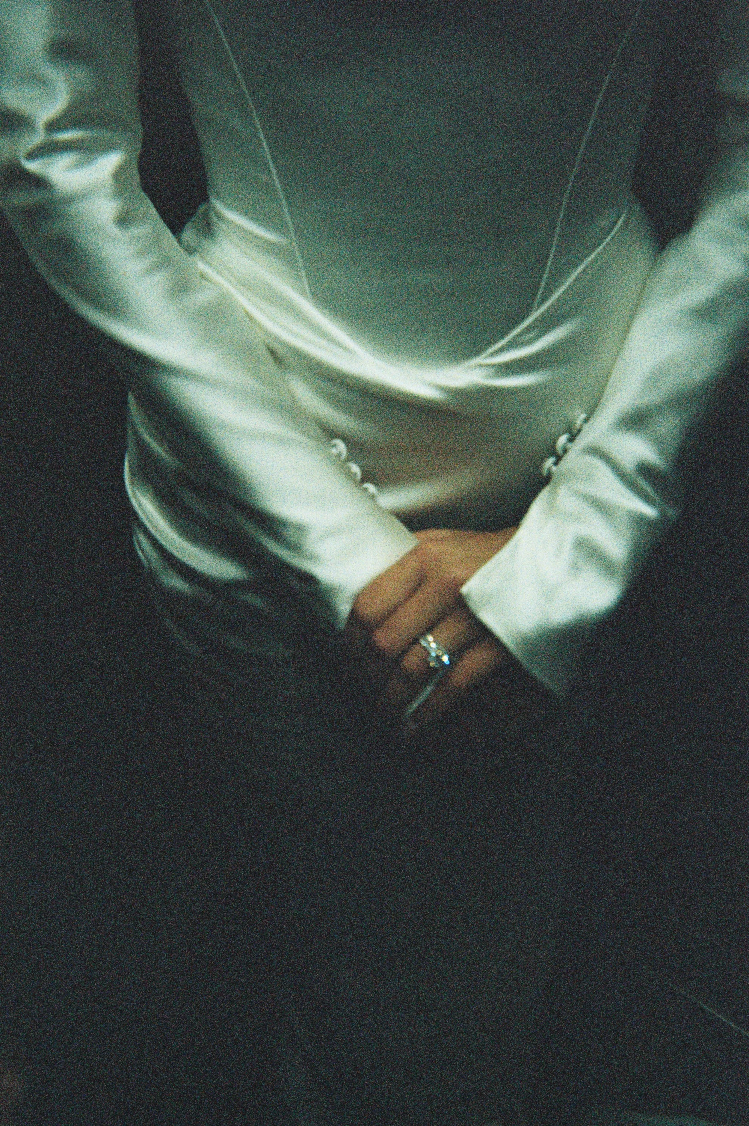 Person wearing a white satin blazer with hands folded, showing a ring on the left hand.