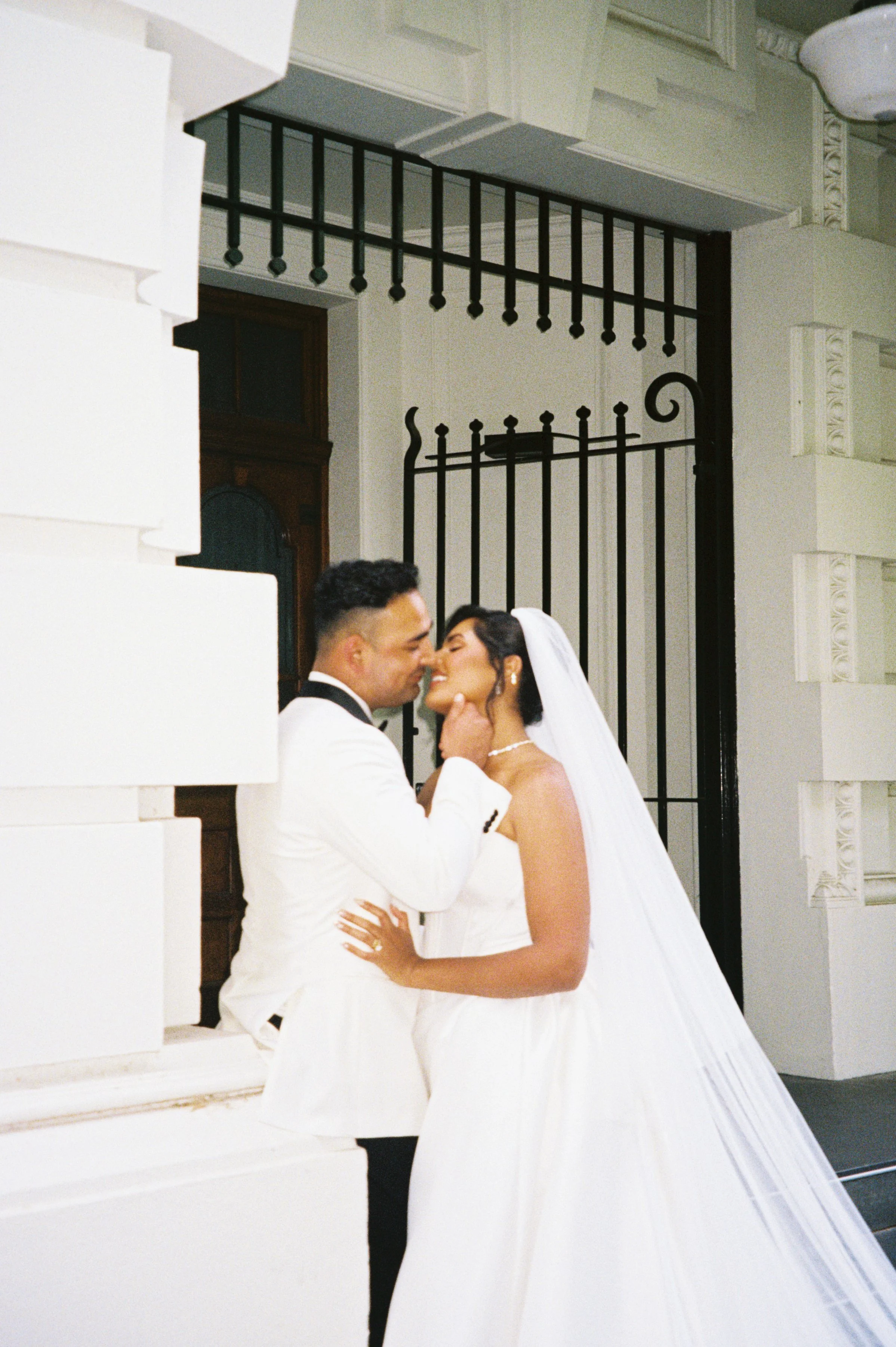 A bride and groom in wedding attire sharing an intimate moment indoors, with the groom gently holding the bride's face.