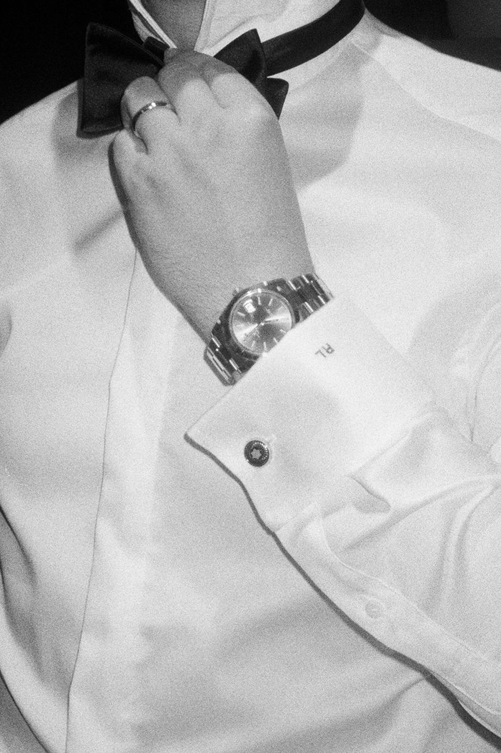 Close-up of a person wearing a wristwatch and cufflinks, adjusting a bow tie with a button-up shirt.