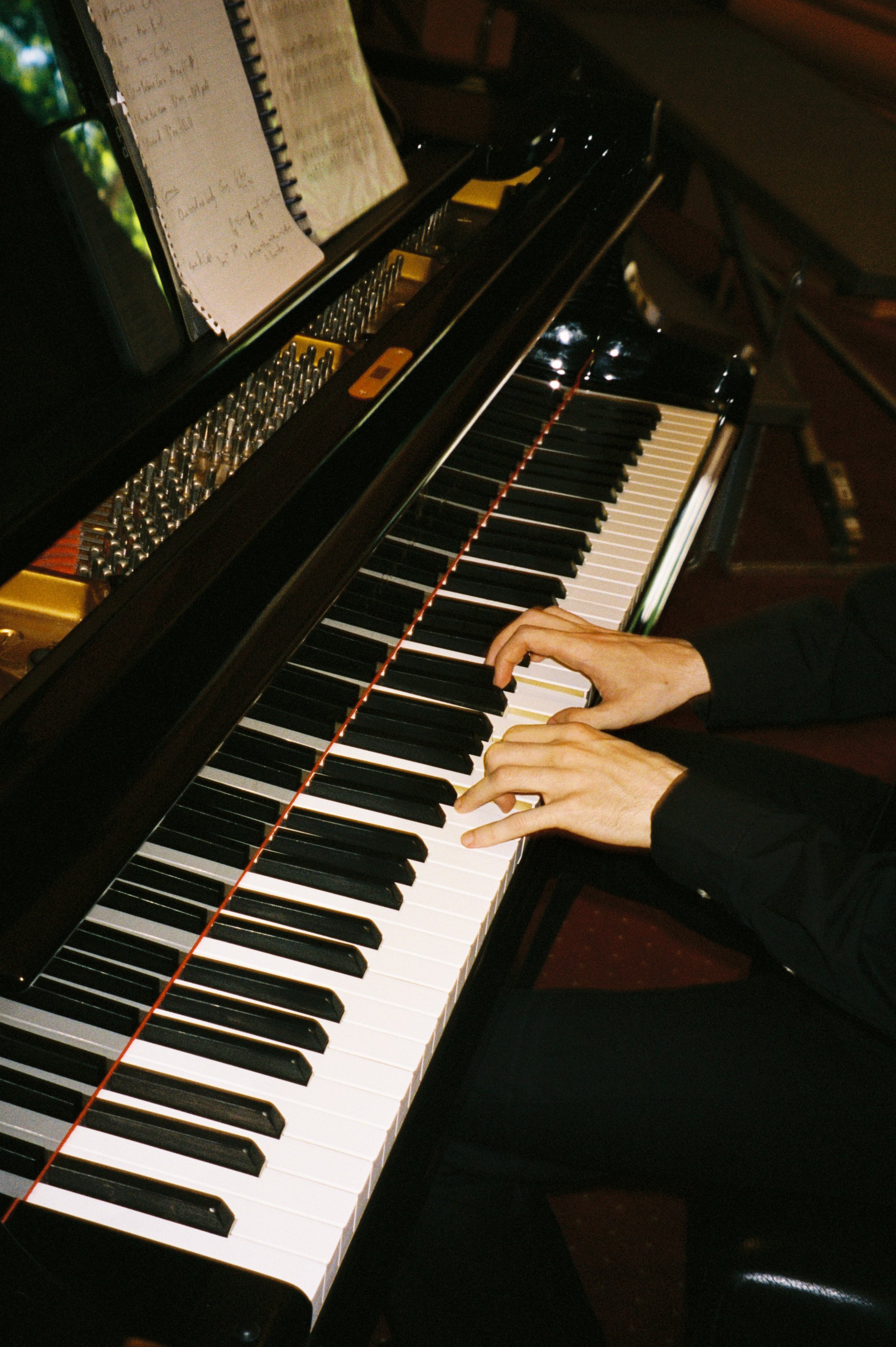 Close-up of a person's hands playing a grand piano, with sheet music and an electronic metronome on the music stand.