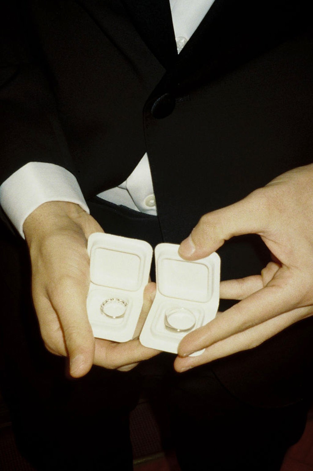 Person dressed in a tuxedo holding open a jewelry box with a wedding ring inside.