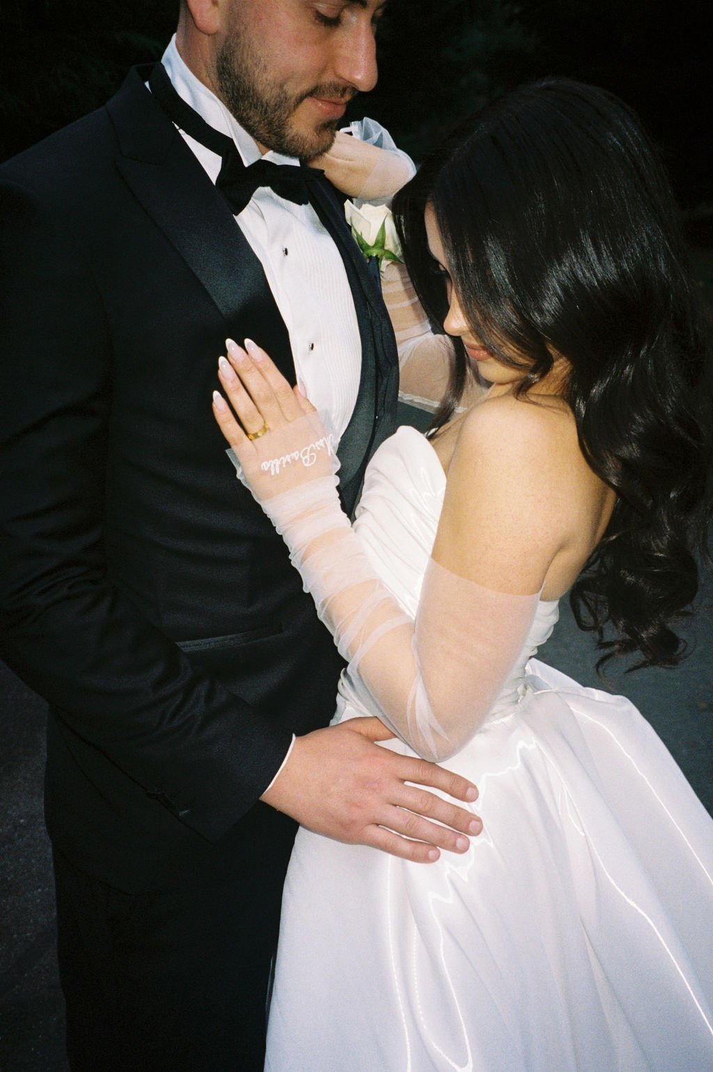 A bride and groom sharing an intimate moment on their wedding day, with the bride wearing a white wedding gown and gloves, and the groom in a black tuxedo with a bowtie.