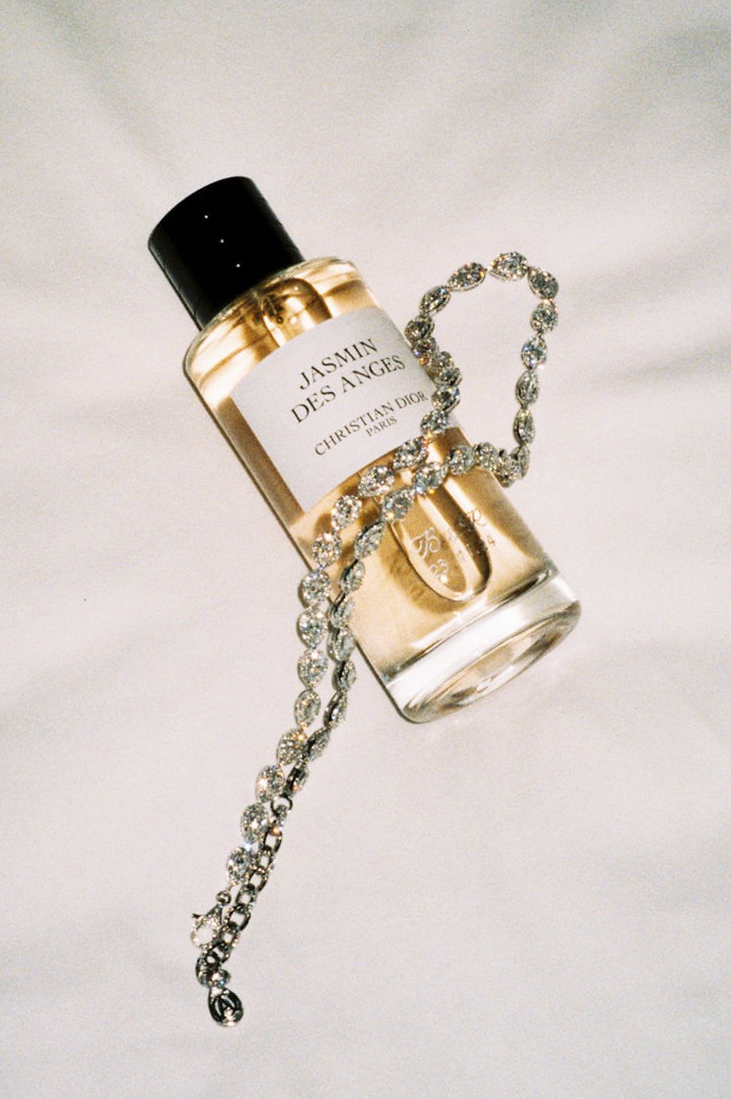 A Chanel No. 5 perfume bottle labeled Jasmin Des Anges with a diamond necklace draped over it on a white surface.
