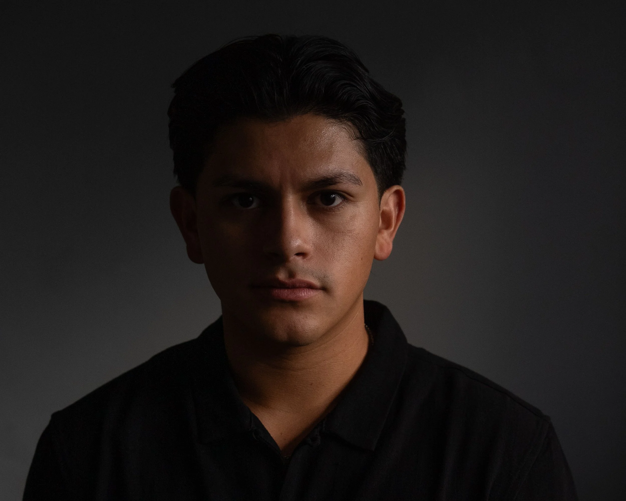 Portrait of a young man with dark hair against a dark background.