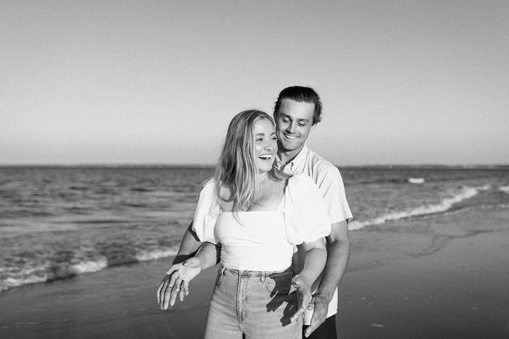 Boyfriend grabbing girlfriend from behind while they laugh on Plum island beach for their beach engagement photoshoot