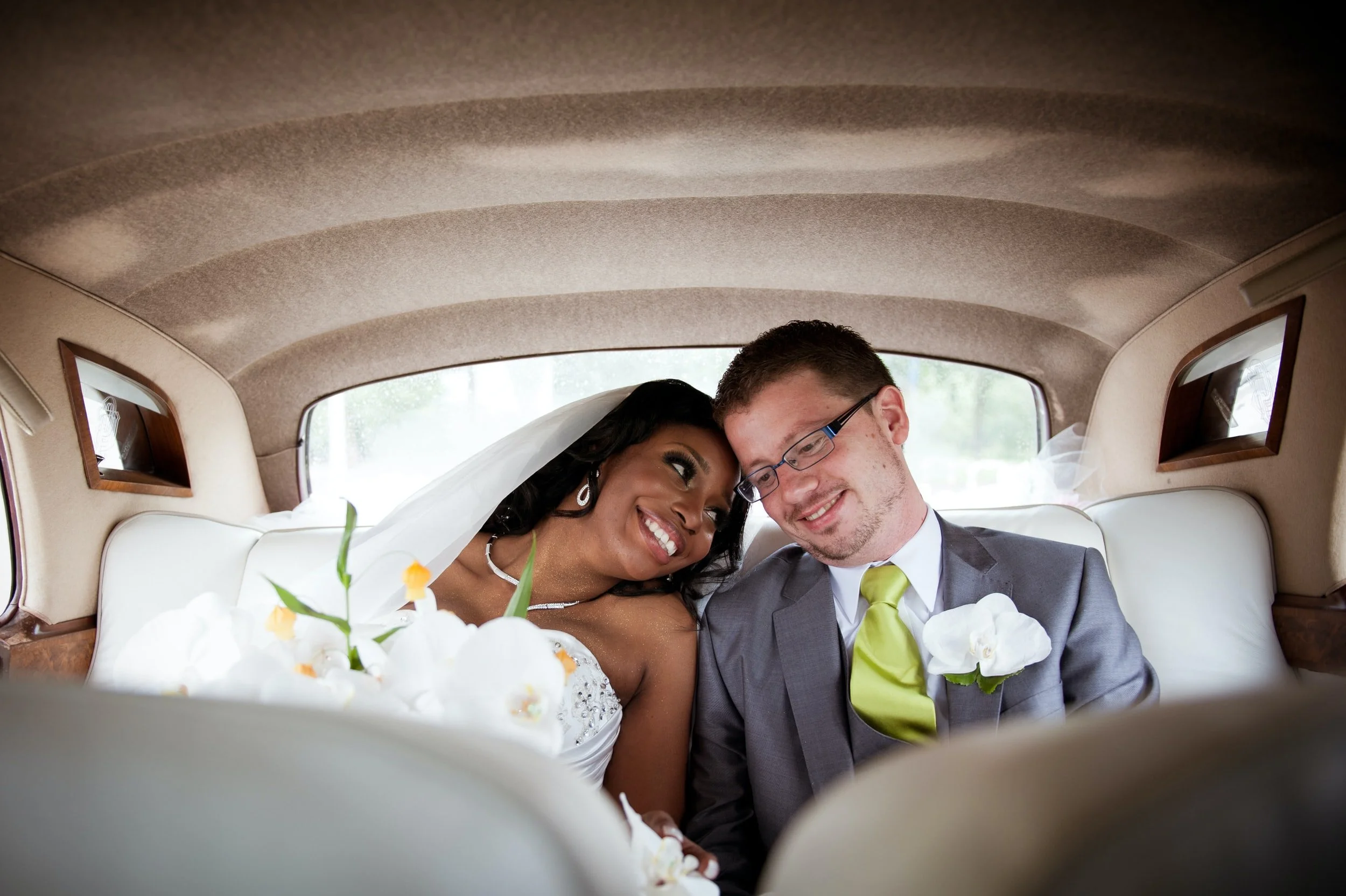 A wedding couple leaning on each other inside a Rolls Royce.