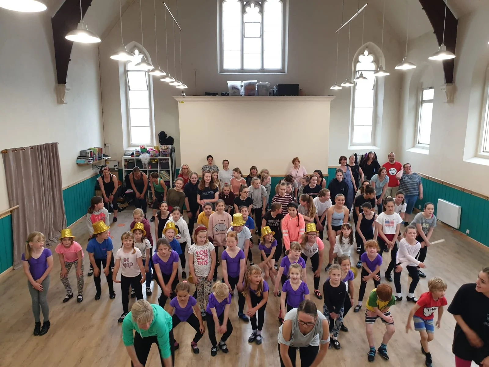 A lively group of dancers of all ages at Just Dance, participating in a high-energy class in a spacious, light-filled studio with a welcoming community atmosphere.