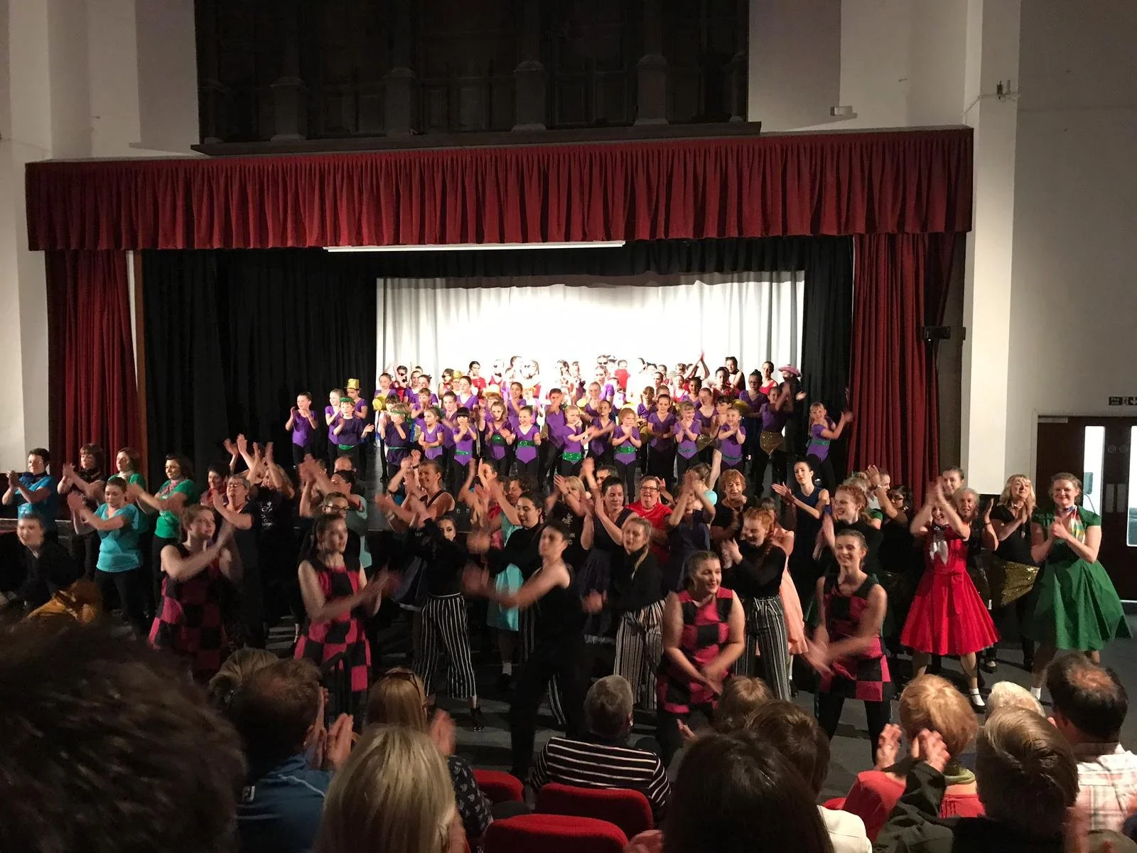 Just Dance performers taking a bow on stage, celebrating a successful production with a full cast and an enthusiastic audience.