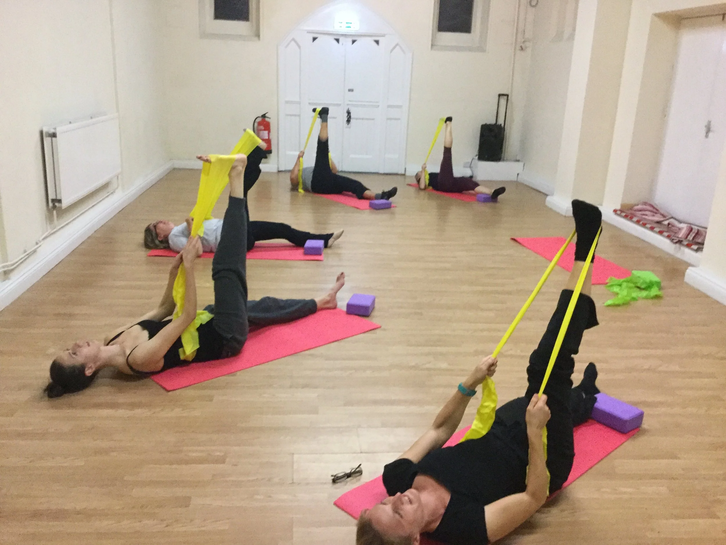 Adult students at Just Dance participating in a stretching and flexibility class, using resistance bands to improve their technique and mobility.