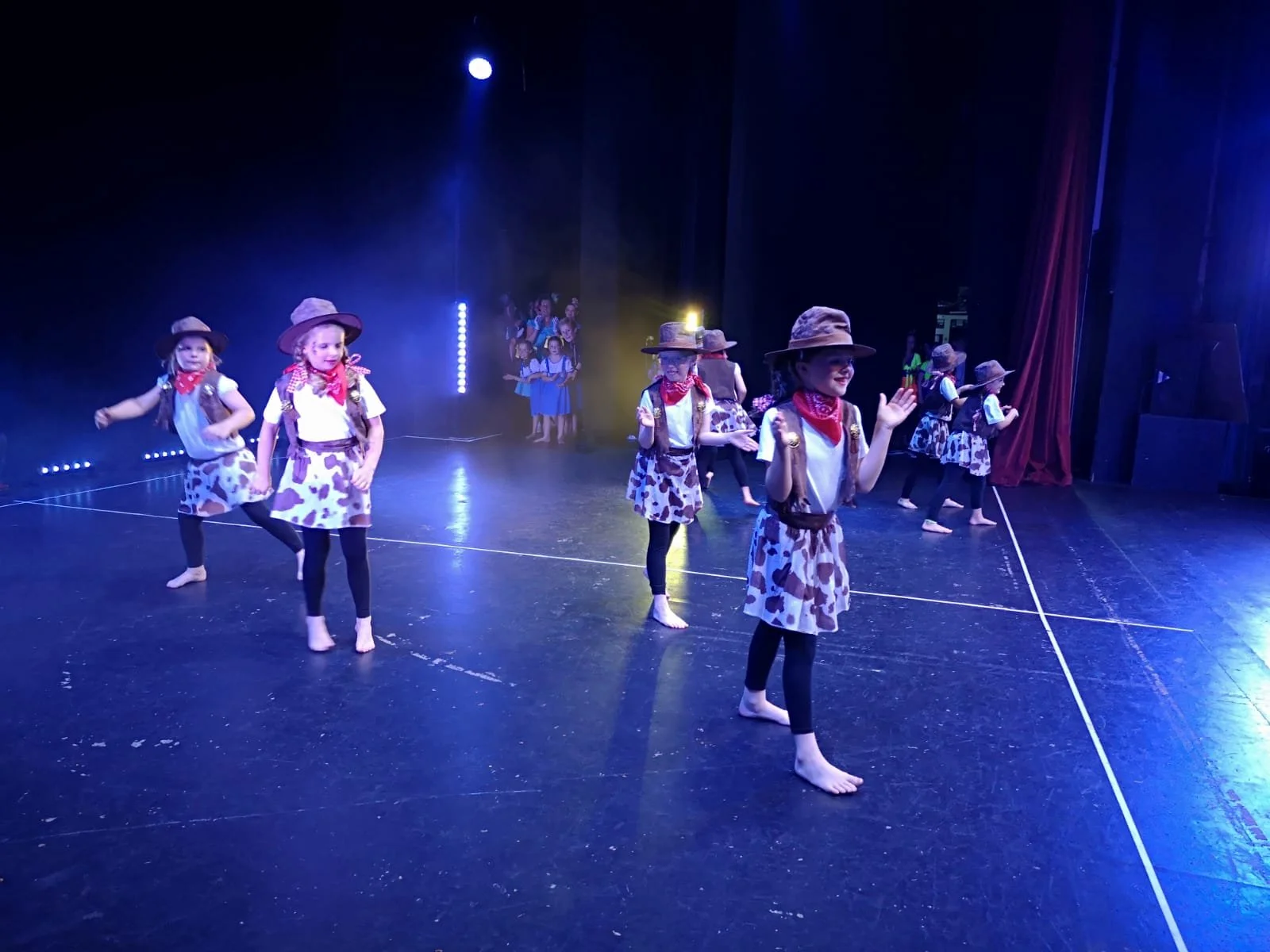A group of young dancers at Just Dance performing on stage in Western-themed costumes, radiating confidence and joy under the spotlight.