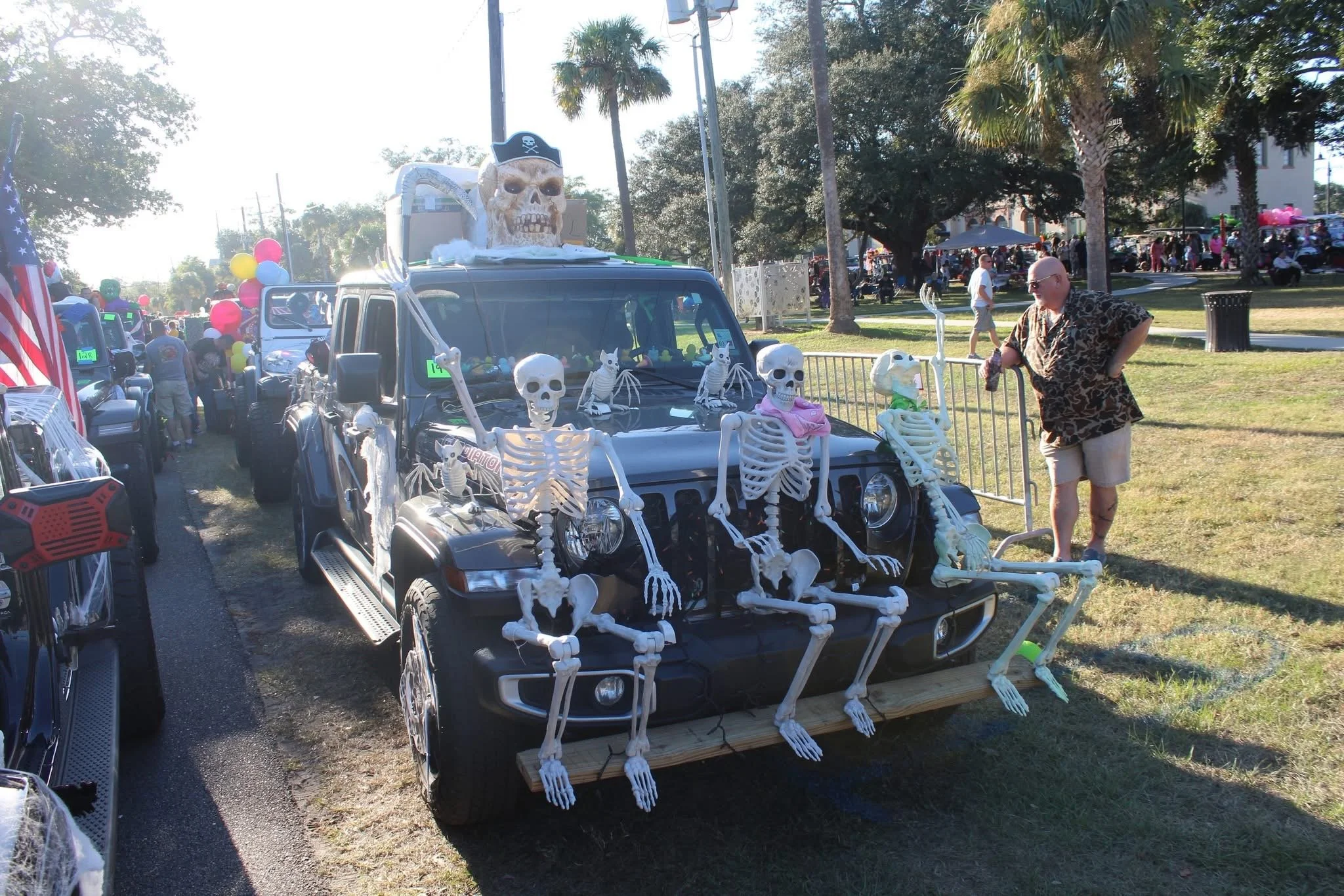 A parade float decorated with skeletons and skulls in front of a crowd, with a large skull with a pirate hat and a flag in the background.