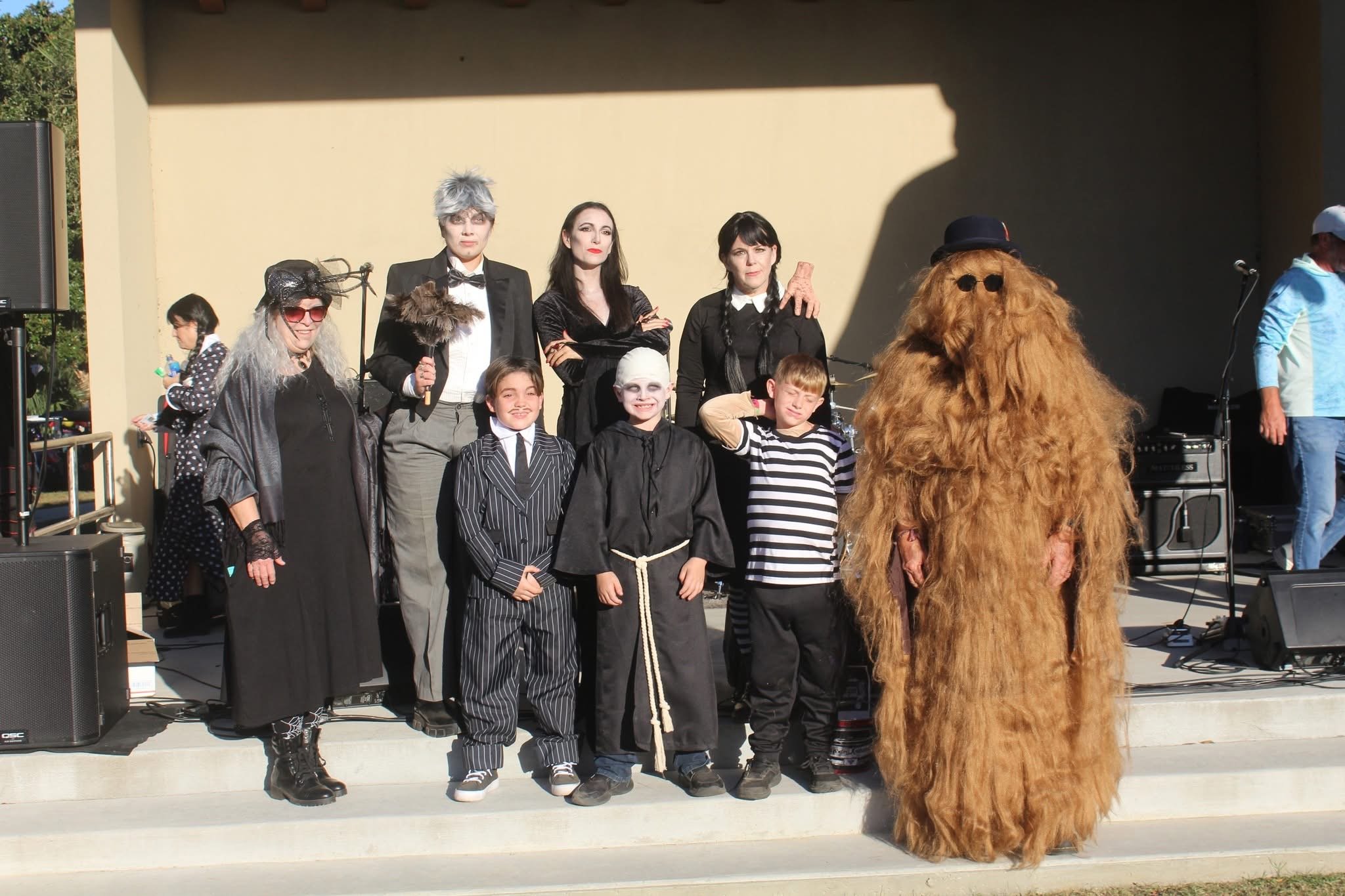 People dressed in costumes, including an animal costume, gathered on a stage outdoors for a performance or event.