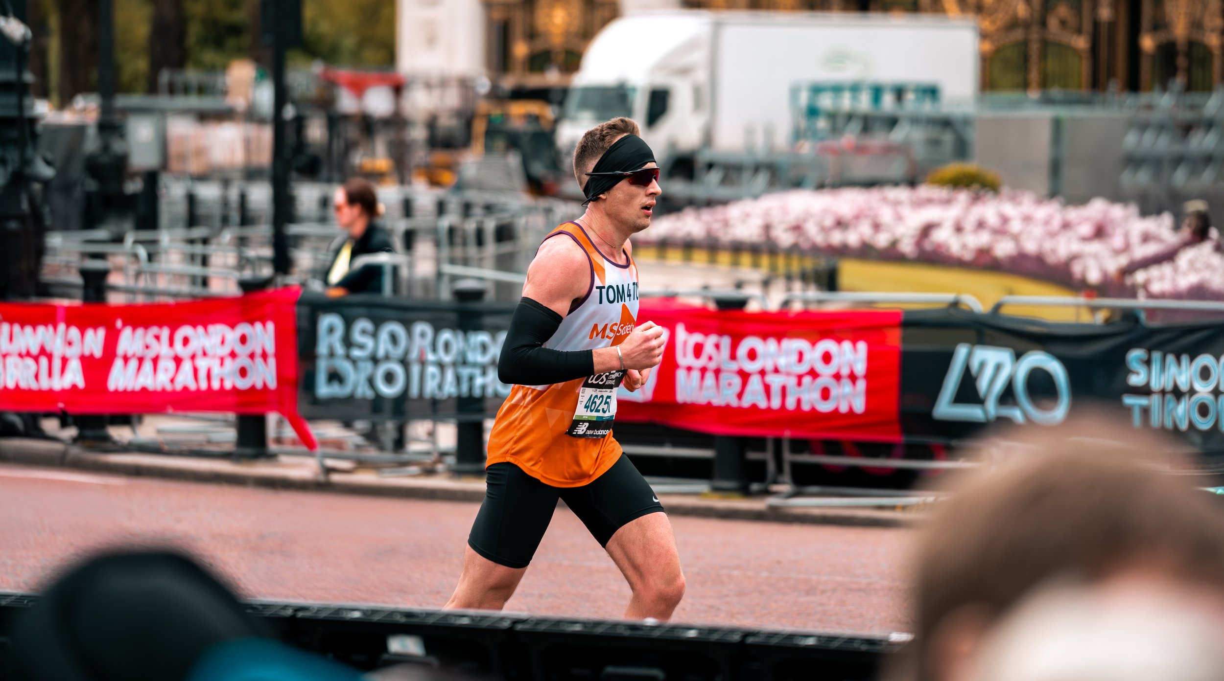 Runner in orange and black participating in London Marathon with spectators and event banners in the background.