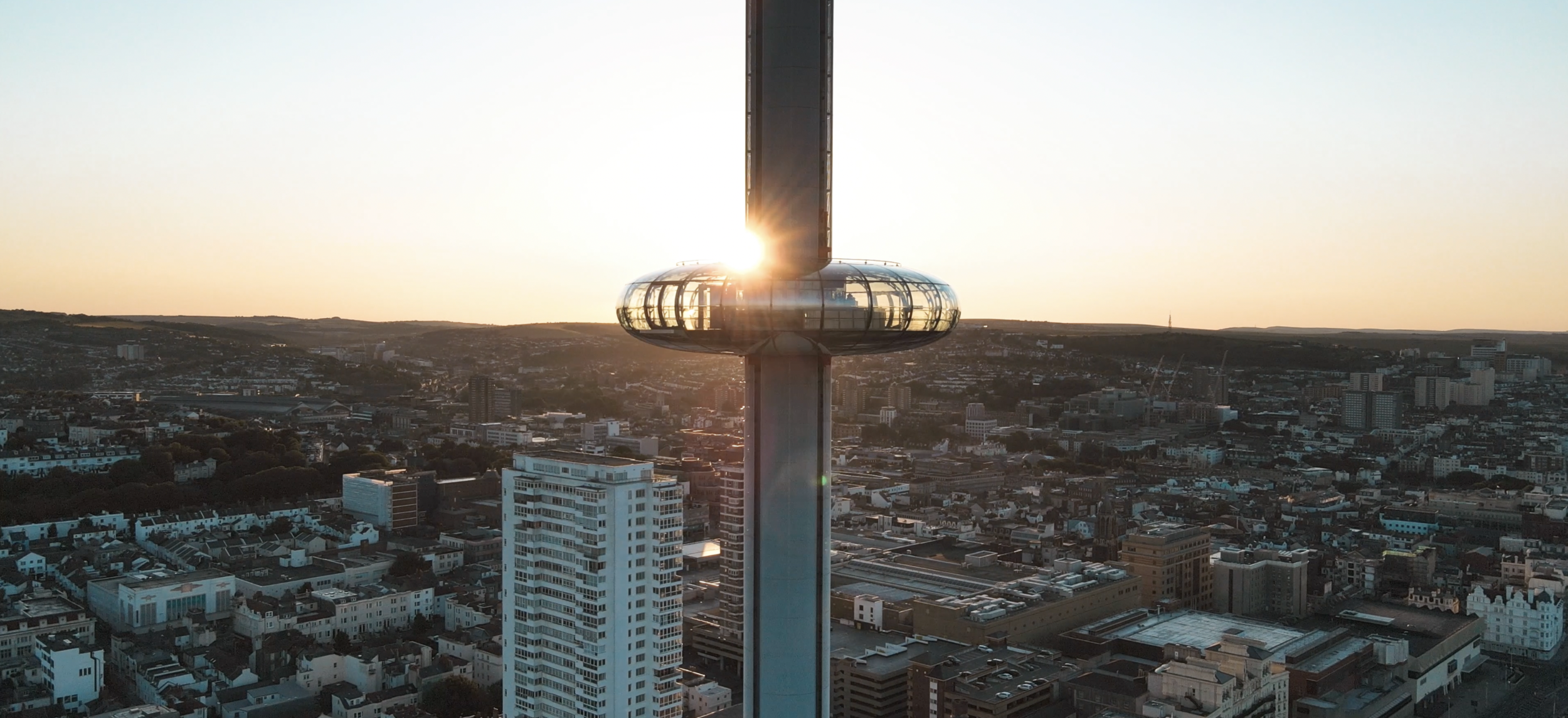 Sunset behind tall observation tower with glass pod, overlooking city skyline.