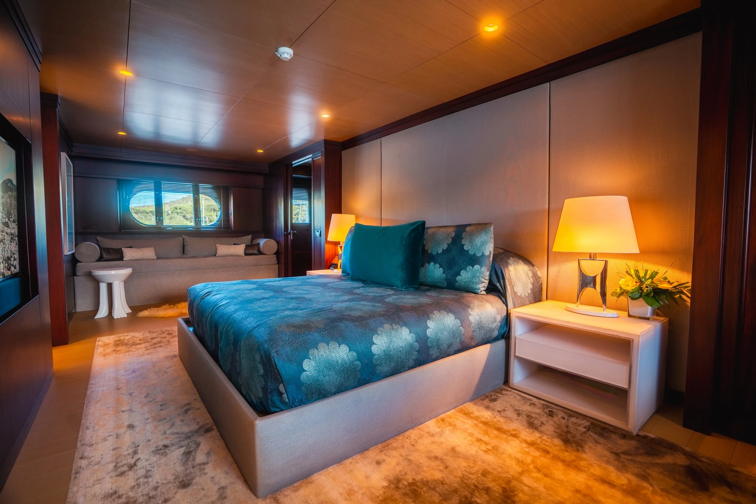 Luxurious bedroom interior with teal bedding, bedside lamp, and window view.