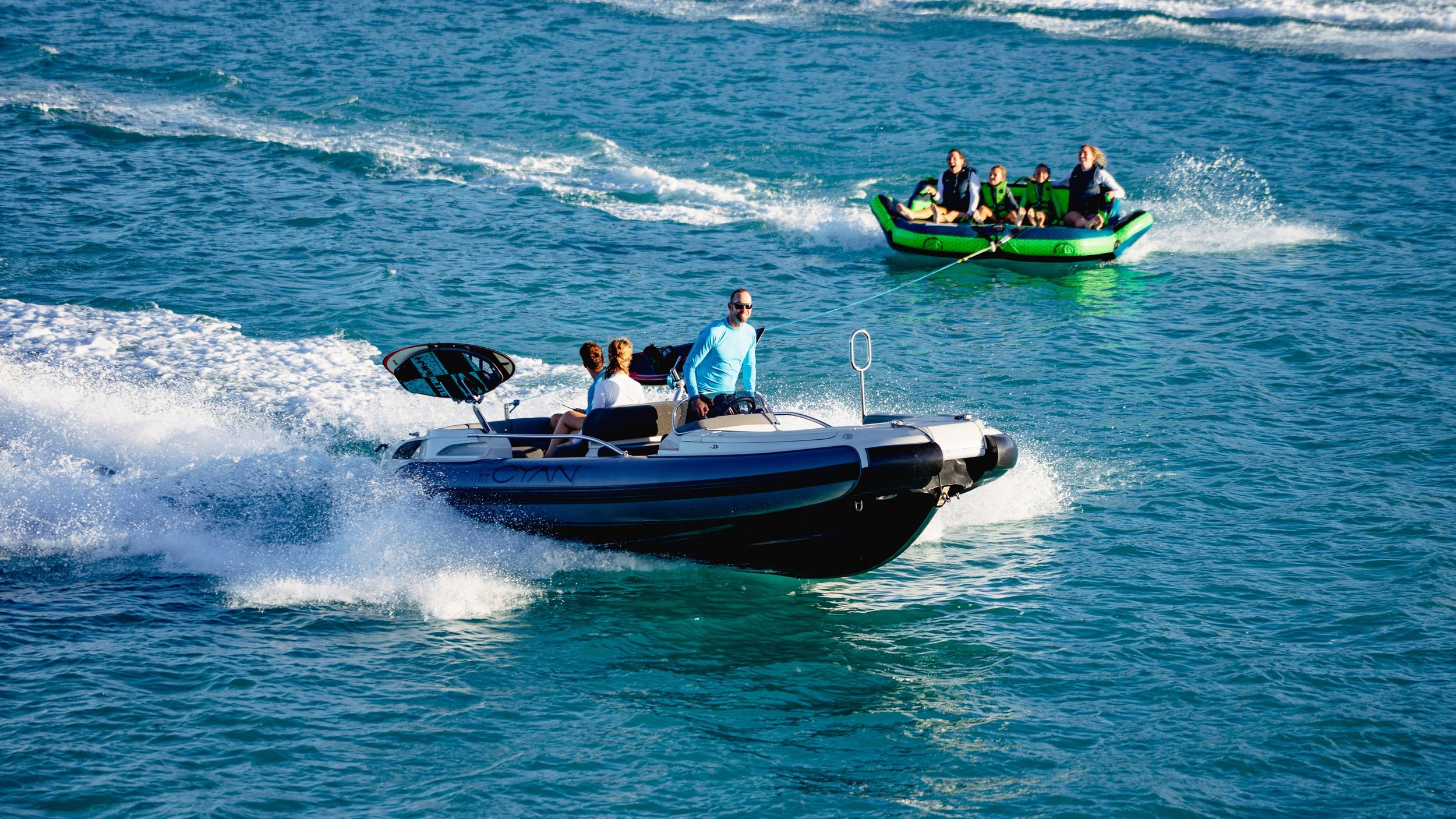 A speedboat pulling a green inflatable tube with people on it over the water.