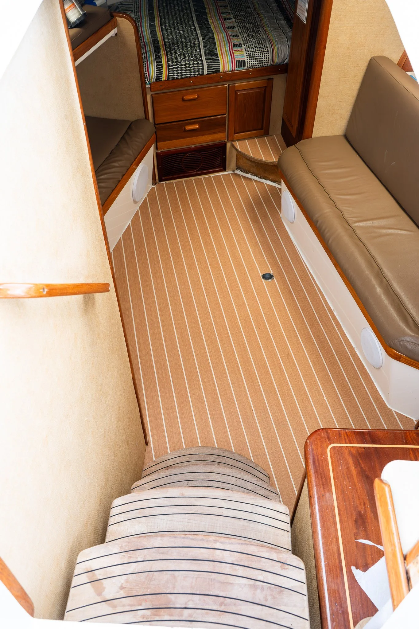 View of the interior of a boat cabin with a small bed, a sofa, and wooden furniture, including a cabinet, and a striped carpet on the floor.