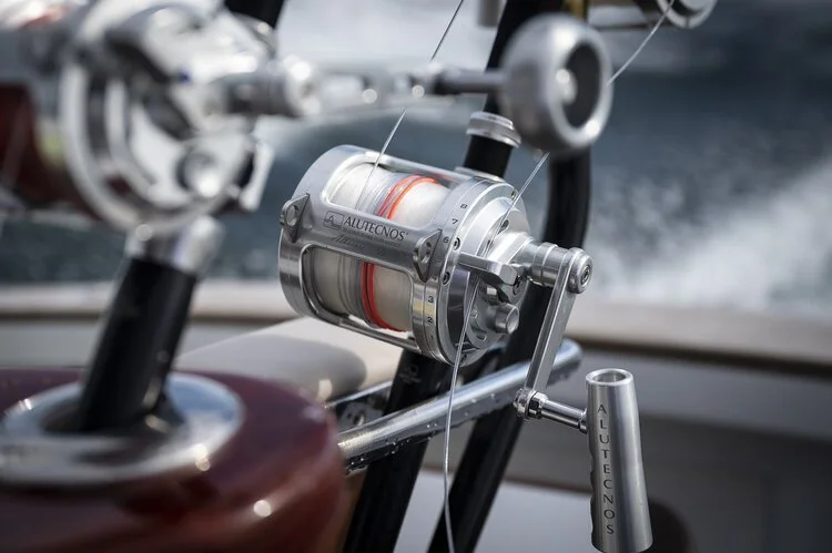 Close-up of a fishing reel mounted on a rod, with a body of water in the background.