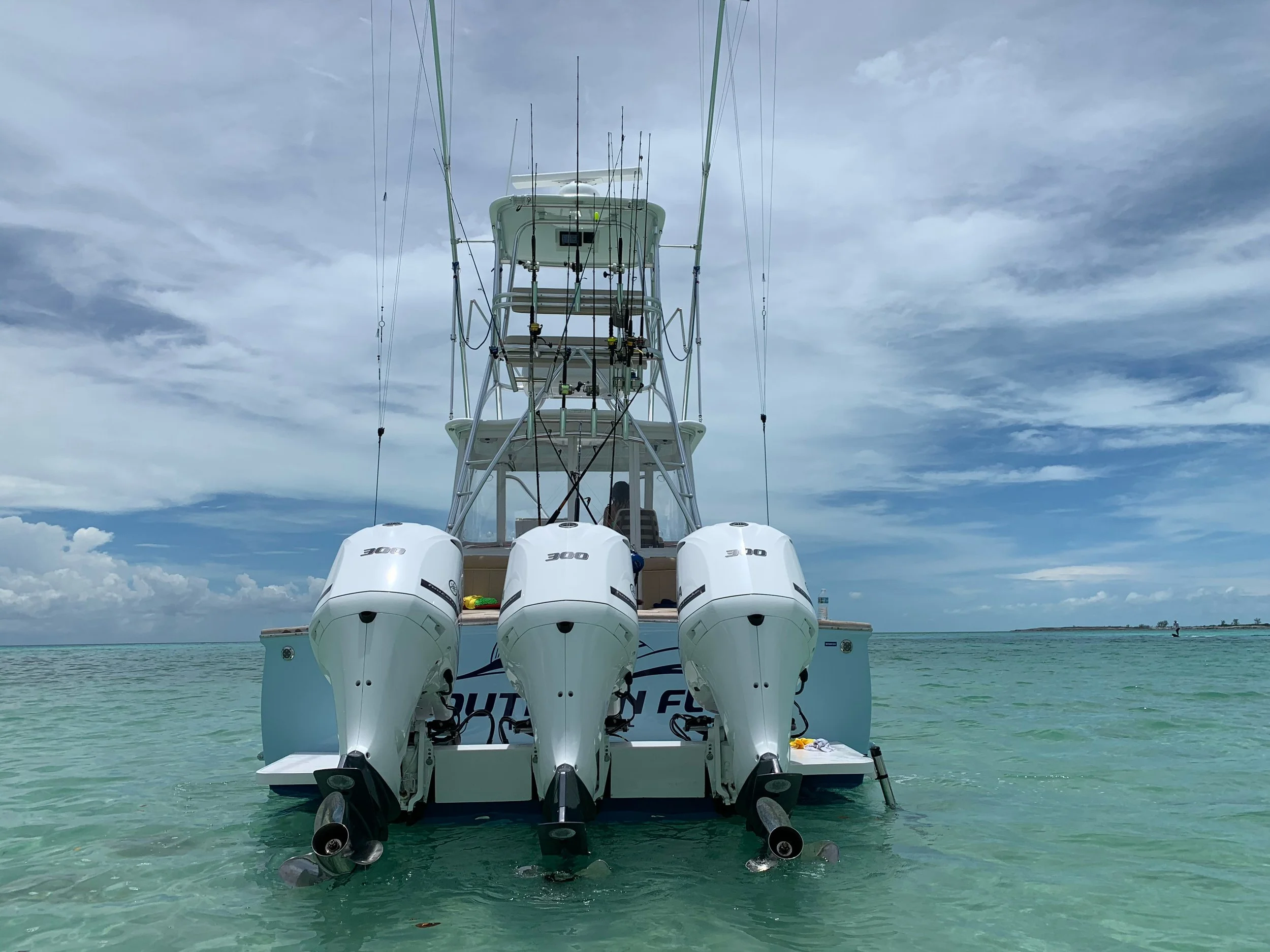 A boat with three outboard motors on a calm, clear ocean under a partly cloudy sky.