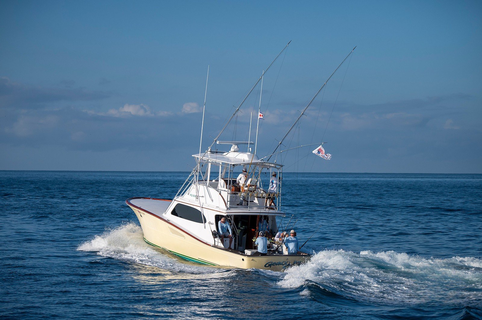 A white fishing boat with multiple anglers on board sailing on the ocean under a partly cloudy sky.