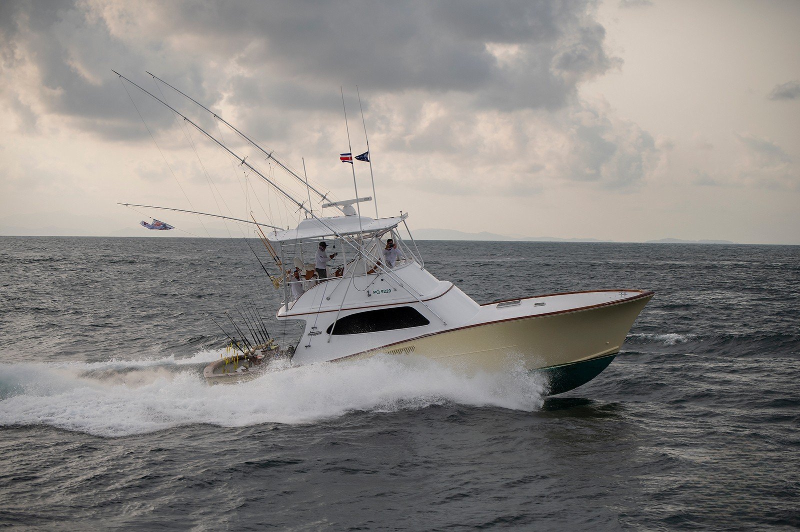 Powerboat speeding through the ocean with fishing rods attached, under cloudy skies with a distant shoreline on the horizon.