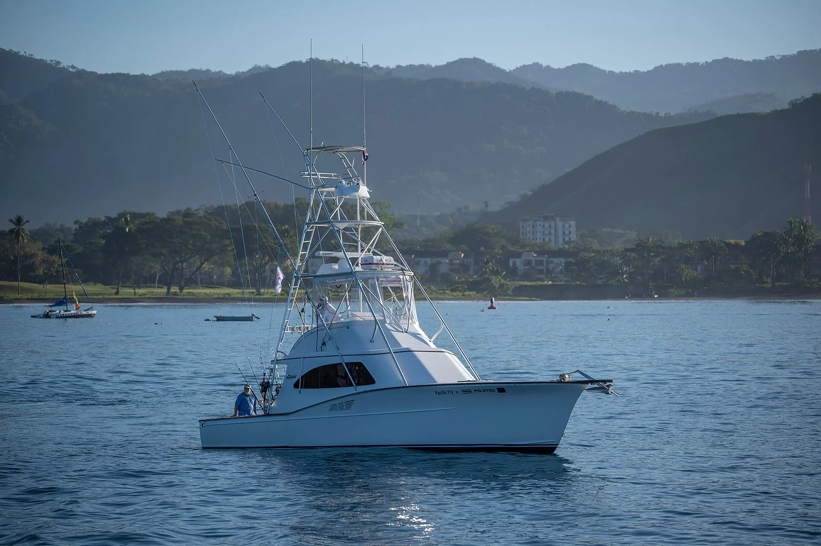 A white fishing boat on calm water with mountains and trees in the background.