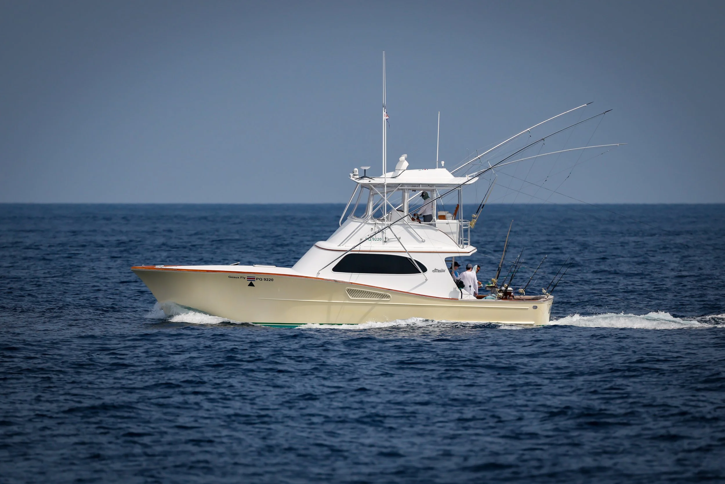 A white fishing boat on the open ocean with multiple fishing rods and two people onboard.