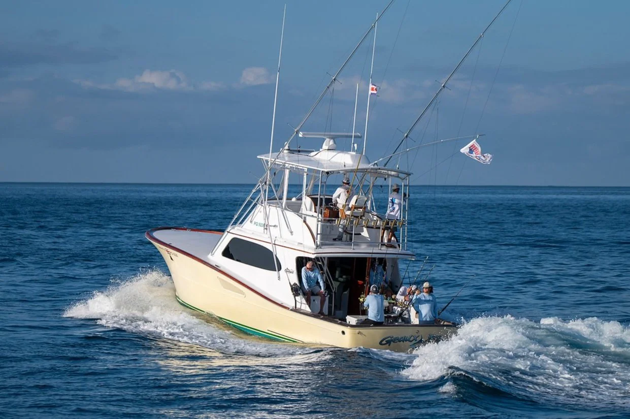 A group of people fishing from a white boat in open water under a partly cloudy sky.