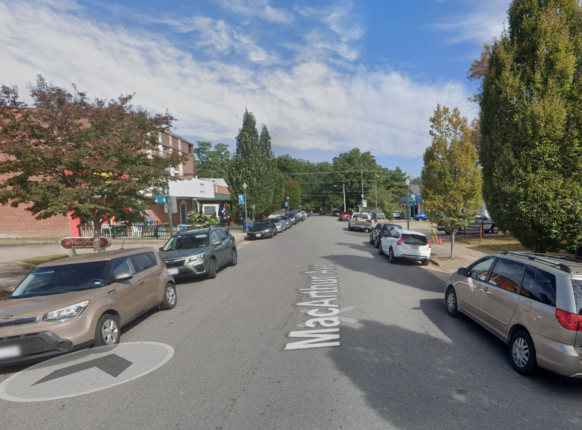 Sports massage therapist Richmond VA. A street view of a small town with parked cars lining both sides of the street, trees with green and autumn-colored leaves, and a business with a sign that reads 'MacArthur'. The sky is partly cloudy.
