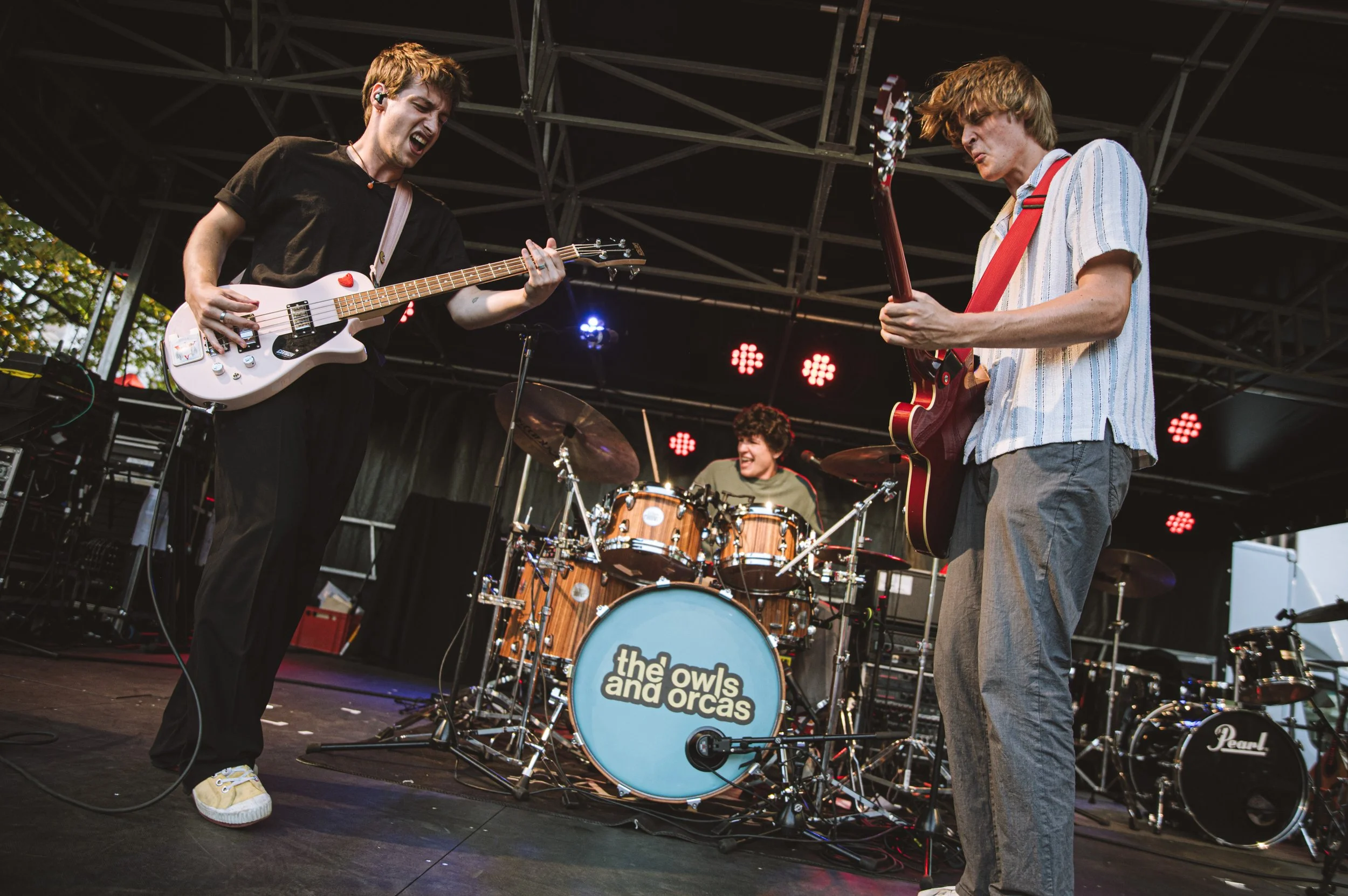 Silhouettes of a band performing on stage with guitars and drums, under foggy lighting, audience in foreground.