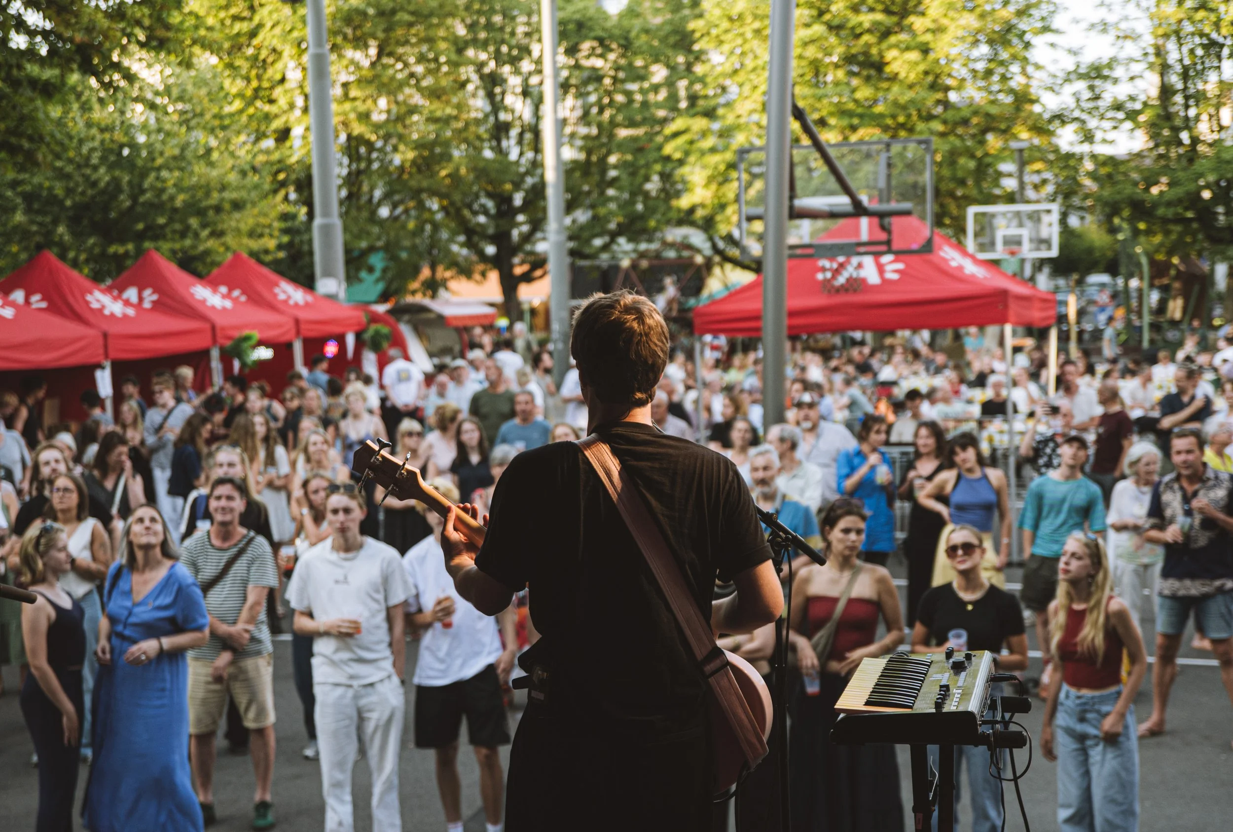 Silhouettes of three musicians on stage with musical instruments and equipment, backlit by bright stage lights in a dark setting.