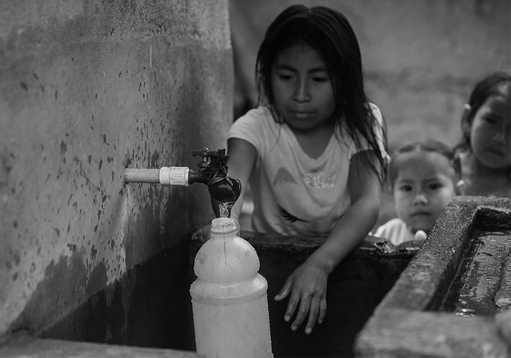 Children collecting water from a household tap in a rural Central American community.