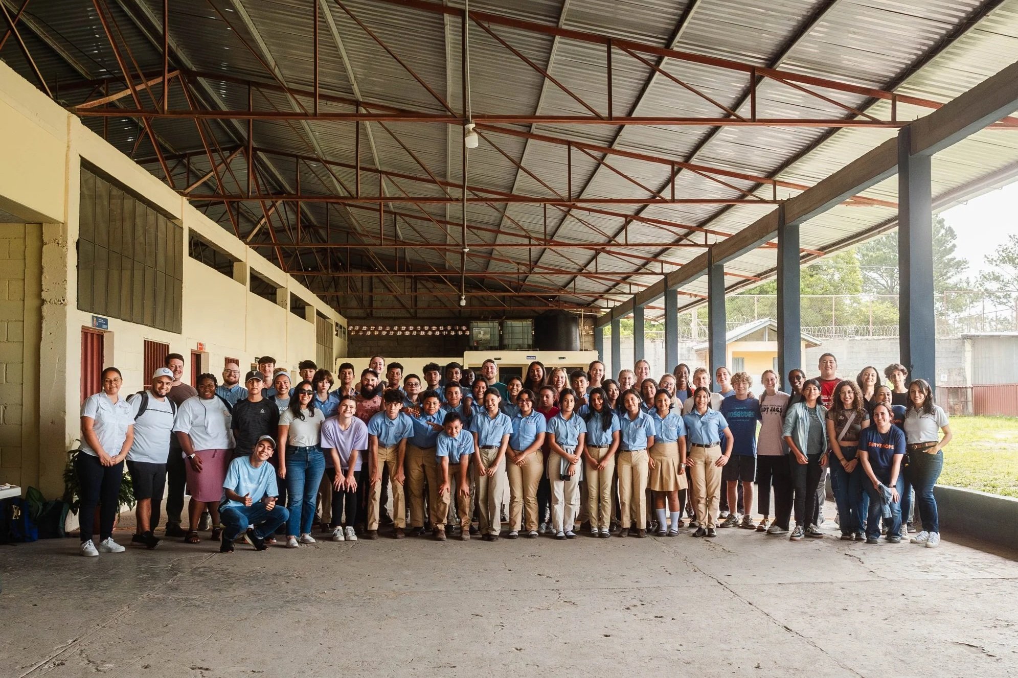 A group of students and teachers stand together under a large school pavilion, symbolizing community and access to education in rural Honduras.