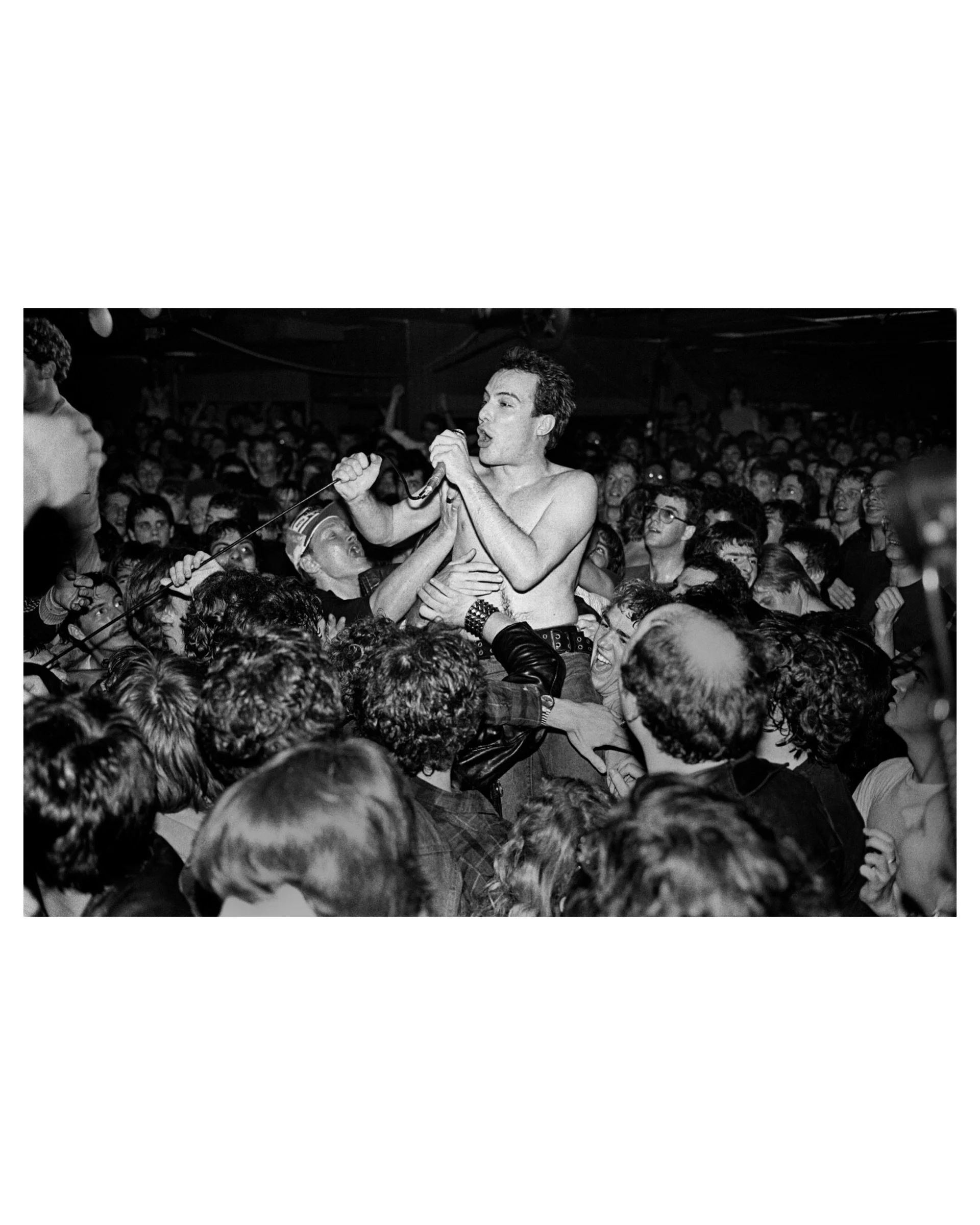 Black and white live concert photo by Michael Grecco of The Dead Kennedys performing while held up by the crowd.