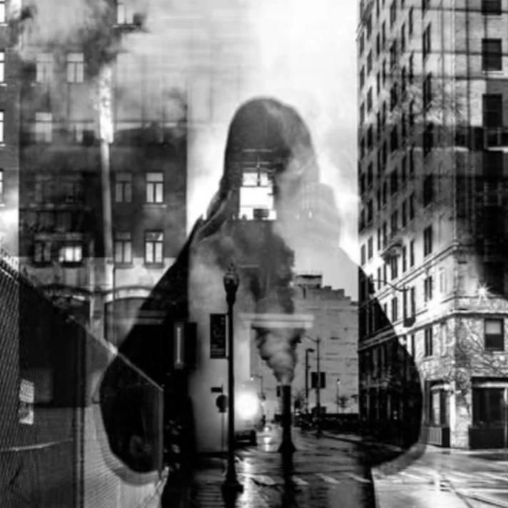 Black and white photo of a city street with tall buildings and streetlights, overlaid with the reflection of Amy Sacka taking a photo, creating a layered, artistic effect.
