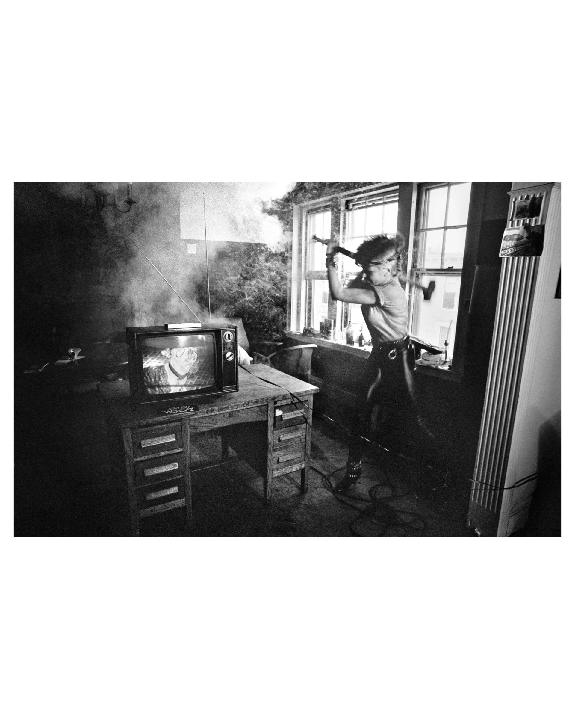 Black and white photo by Michael Grecco of Wendy O. Williams smashing a television with a bat in a smoke-filled room.