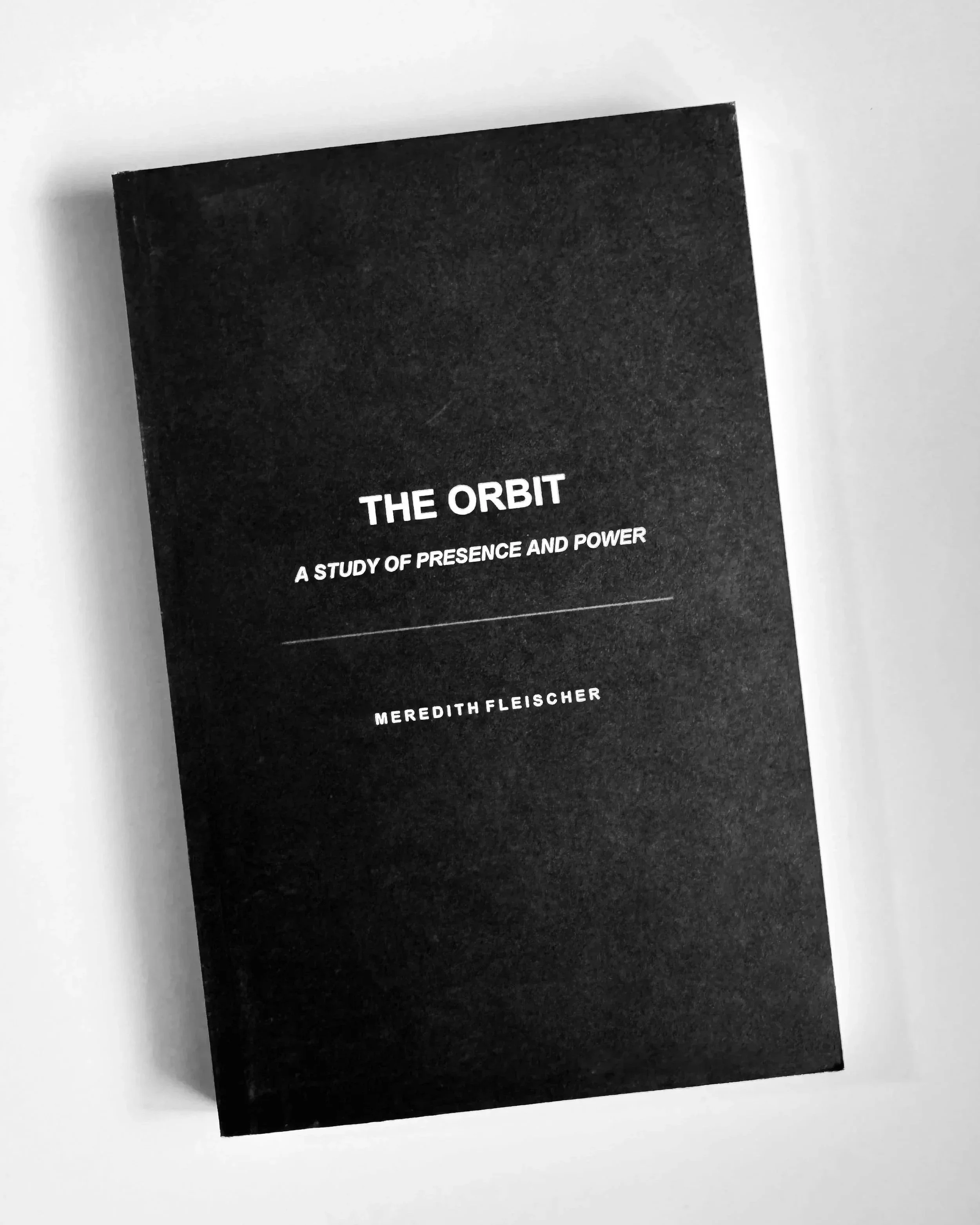 A black book titled 'The Orbit' with the subtitle 'A Study of Presence and Power' by Meredith Fleischer, placed on a white surface.
